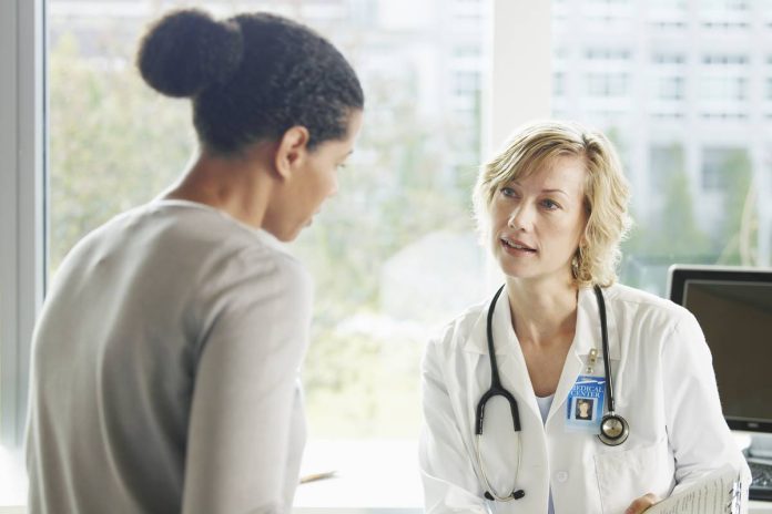 Foto colorida - Duas mulheres, uma com roupa de médica e outra com roupa comum