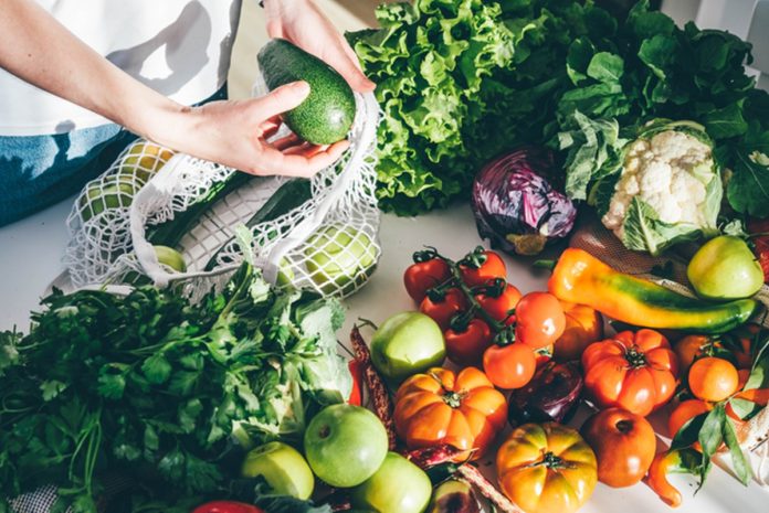 Foto colorida de mulher segurando abacate em mesa com vegetais - Metrópoles - dieta