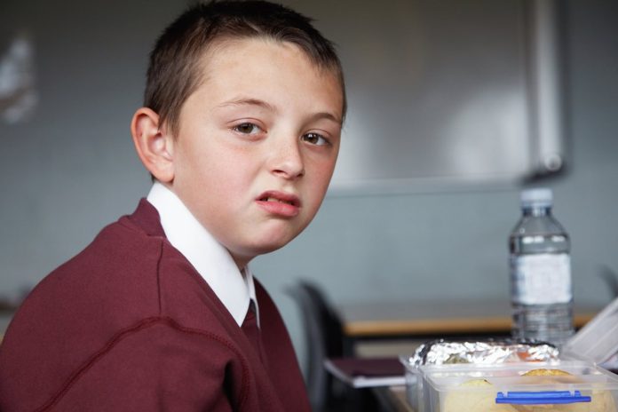 Foto colorida de menino de pele clara, com cara feia, olhando para a câmera, vestido com blusa roxa - Metrópoles