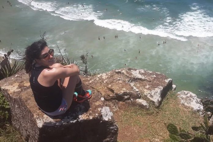 Personagem lívia em 2014. Ela está sentada em pedras e ao fundo é possível ver o mar.