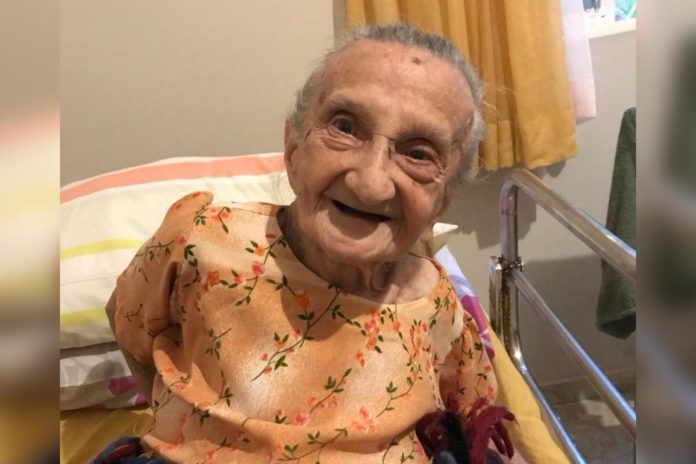 Foto colorida de idosa vestida com blusa florida de cor laranja enquanto sorri - Metrópoles.