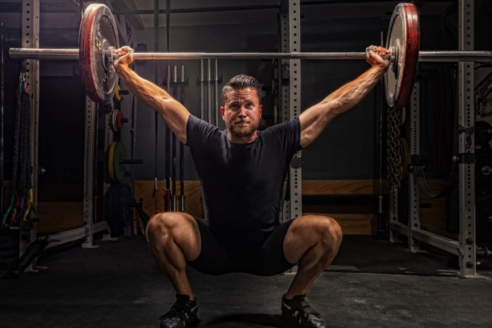 Homem de pele clara levantando peso com as mãos acima da cabeça - Metrópoles. 